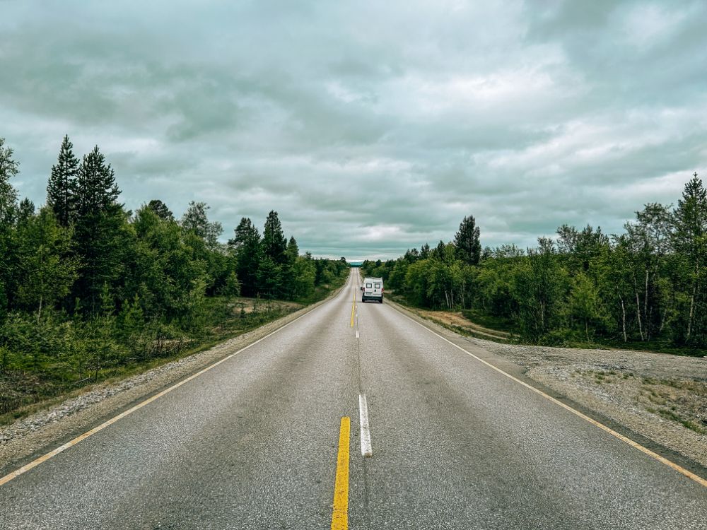 Furgone mentre percorre una strada in Finlandia che taglia una foresta di pini e betulle