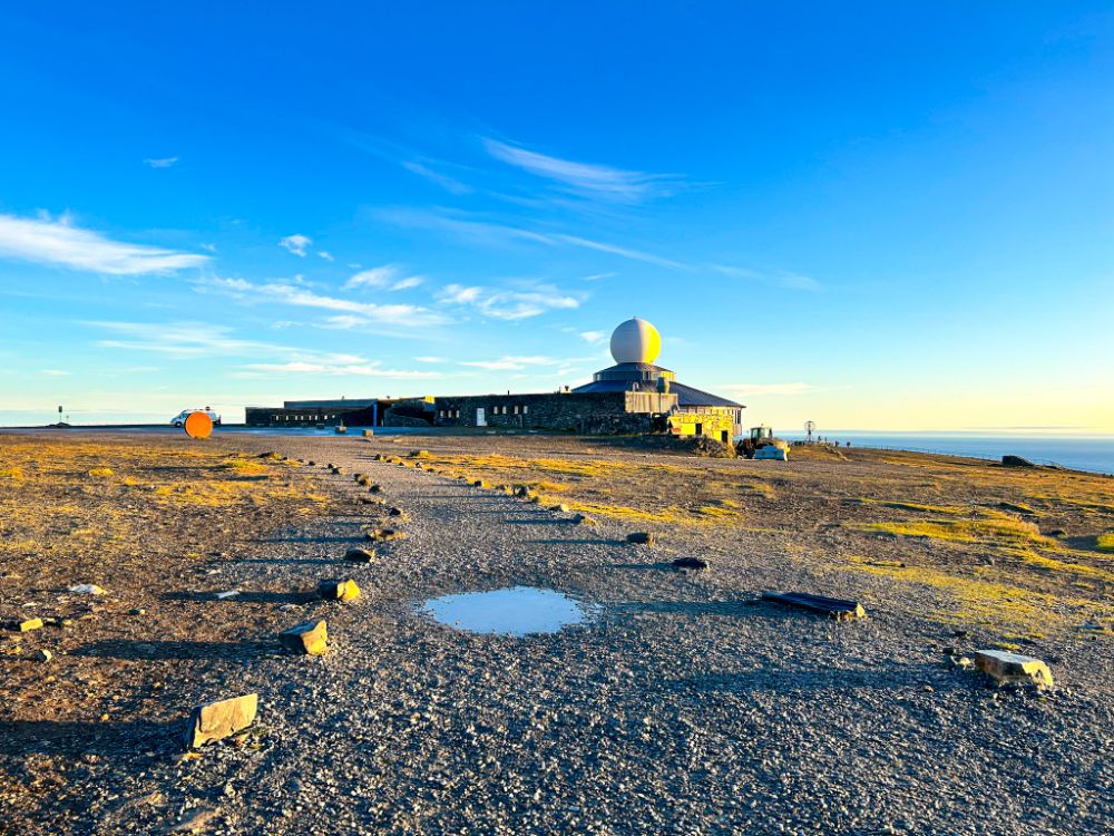 Il centro visitatori Nordkapphallen a Capo Nord, Norvegia. Si vede un sentiero sterrato che conduce alla struttura moderna caratterizzata da una grande cupola bianca (radome), situata su un altopiano spoglio sotto un cielo azzurro e limpido.