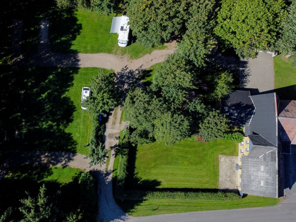 Vista dall'alto di un giardino con alberi, una casa e un paio di camper parcheggiati.